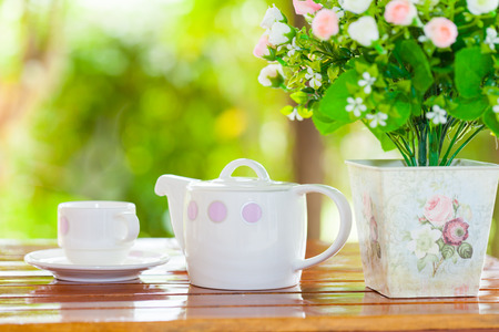 White porcelain set for tea or coffee on wooden table in the garden over blur green nature background, shallow DOF teapot in focusの写真素材