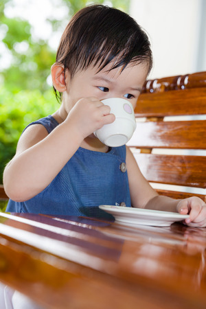 Little asian girl (thai) drinking from a cup at home exterior in relax timeの写真素材