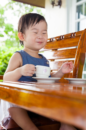 Little asian girl smiling and holding a teacup at home exterior in relax timeの写真素材
