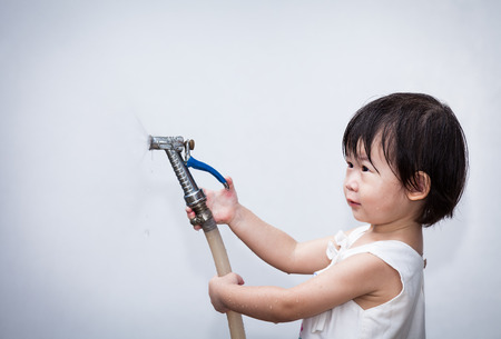 Adorable little asian (thai) girl play with water hose on wall white backgroundの写真素材