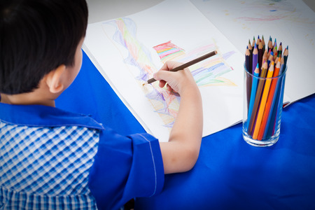 Little asian boy sitting at the table and drawing by colour pencil, shot in studioの写真素材