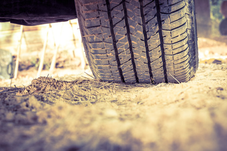 Closeup car tire on the ground. Wheel tracks on dirt, shallow depth of field (DOF) tyre in focus. Vintage picture styleの写真素材