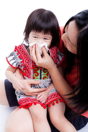 Asian mother wipes snot her daughter. Little girl with allergy symptom and sitting on young woman lap. On white backgroundの写真素材