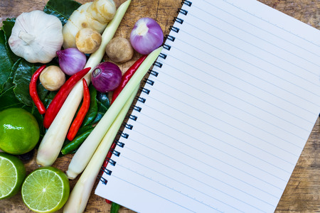 Close up. Open notebook with kaffir lime leaf, lemon, lemongrass, galangal, chili, onions and Straw mushroom herb and spicy ingredients Thai food (tom yum) on wooden background.の写真素材
