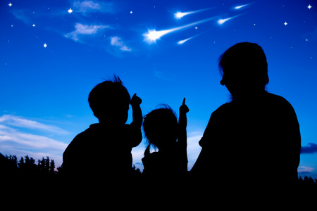 Silhouette of mother and two kids sitting and looking sky at Comets. Little children and parent point to comets. Colorful blue sky background. Friendly family.の写真素材