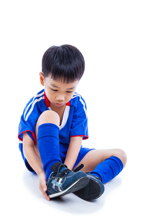 Youth asian soccer player in blue uniform tying shoe before playing soccer with drop shadow.Child preparing ready for competition. Sport lifestyle. Isolated on white background. Studio shot. Full bodyの写真素材