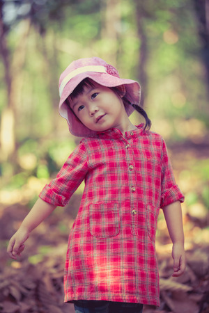 Cute little asian girl playing over garden background. Photo in retro style. Pretty child in nature. Outdoors portrait.の写真素材