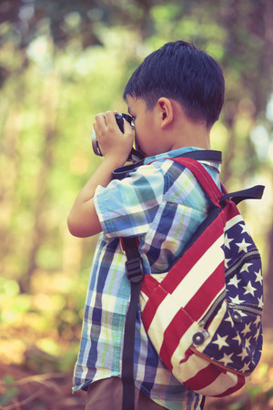 Asian boy taking photos by professional digital camera in garden background. Photo in retro style. Smart child in nature. Outdoors portrait. Photo in retro style.の写真素材