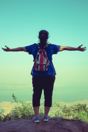 Back view of woman standing on boulder and stretching the arms on vacation. Cross process.の写真素材