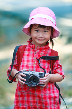 Cute little asian girl with professional digital camera looking at camera and smiling over nature background. Child in nature. Outdoors portrait.の写真素材