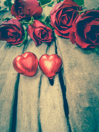 Red roses and two chocolate heart for Valentine's Day on wooden table background. Free form copy space. Vintage picture style.の写真素材