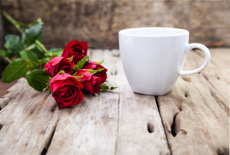 Bouquet of beautiful red roses and coffee cup for Valentine's Day on blurred wooden background. Shallow depth of field (dof), selective focus.の写真素材