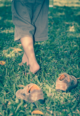 Child take off leather shoes. Close up child's foot learns to walk on grass, reflexology massage. Kid relax in garden. Shallow depth of field (dof), selective focus. Retro style.の写真素材