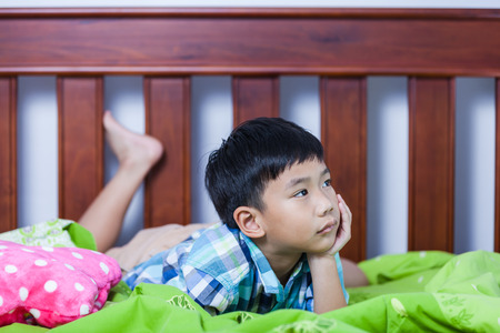 Sad child inside bedroom. Handsome asian boy lying on his bed looking sad and lonely. Problem families concept.の写真素材