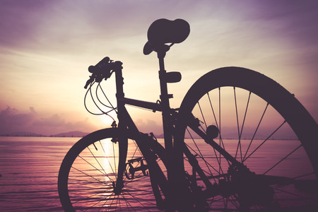 Silhouette of bicycle on the beach against colorful sunset in the sea, purple sky background....