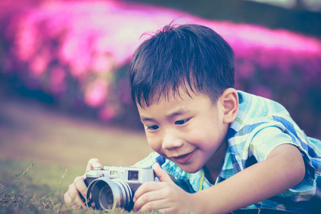 Asian boy taking photo by vintage film camera on blurred nature background at the day time. Vintage picture style.の写真素材
