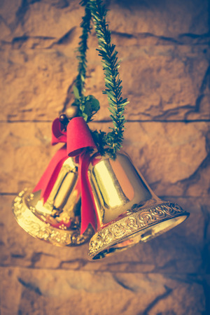 Christmas golden bells with a red bow hanging on the brick wall background. Vintage tone.の写真素材