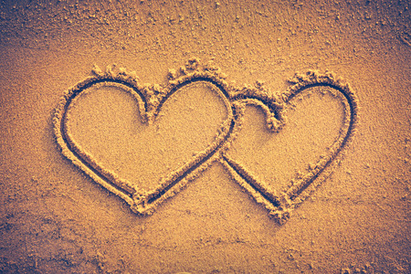 Two hearts handwritten on seashore sand. Valentine's day on the beach. Vignette and vintage picture style. Warm tone.の写真素材