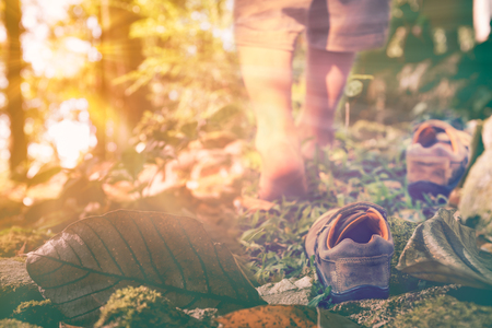 Child take off leather shoes, child's foot learns to walk on grass with bright sunlight, reflexology massage. Kid relax in park on vacation. Shallow depth of field (dof), selective focus. Retro style.の写真素材