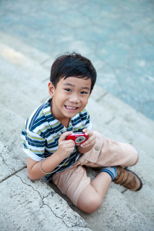 Happy asian boy with camera at park. Child relaxing outdoors in the day time, travel on vacation. Positive human emotion.の写真素材