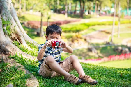 Asian boy trying to take photo by camera on nature background. Child relaxing outdoors in the day time at park, travel on vacation. Positive human emotion.の写真素材