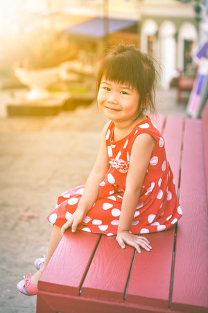 Happy asian girl smiling and looking at camera. Child relaxing outdoors in the day time with bright sunlight, travel on vacation. Positive human emotion.の写真素材