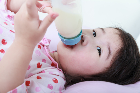 Closeup cute asian girl sucking up milk bottle in bed. Drinking milk for good health.の写真素材