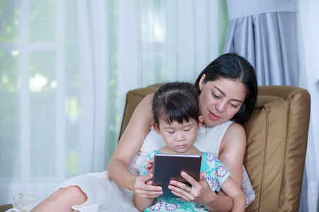 Asian girl using digital tablet with her mother near by. Child finger point at tablet. Family spending time together at home. Concept about education by e-learning.の写真素材