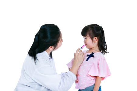 Caring medical doctor giving child medication by syringe. Sick child taking syrup against flu. Happy pediatrician and asian girl smiling together. Children health concept. Isolated on white background.の写真素材