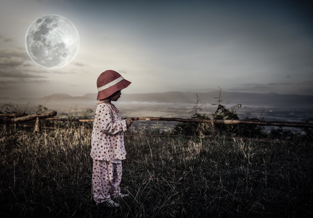 Asian child relaxing outdoors with bright full moon at night, travel on vacation. Adorable girl in night sky under beautiful full moon. Vintage tone effect. The moon were NOT furnished by NASA.の写真素材