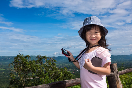 Happy asian girl smiling at view point on mountain. Child learning take photographs landscape blue sky and cloudy nature background. Child relaxing outdoors at the daytime, travel on vacation.の写真素材