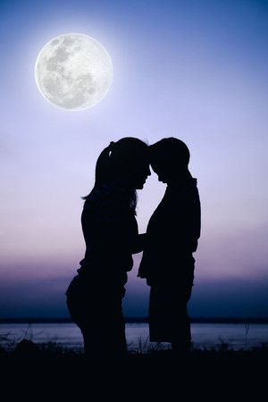 Silhouette side view of mother and child enjoying at riverside. Mother hugging her son on colorful sky background. Friendly family. Cool colors tone photo effect.の写真素材