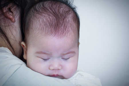 Mother and baby. Lovely asian girl sleeping and resting on her mother's shoulder. Happy family spending time togetherness. Mother's Day celebration. Vignette picture style.の写真素材