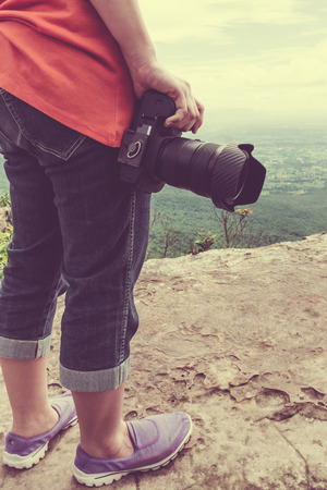 Woman with digital camera at view point on mountain. Outdoor at the daytime on summer day. Travel lifestyle vacations concept. Vintage tone effect.の写真素材