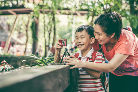 Portrait of young asian mother smiling and teaching her son photographing outdoors using digital camera. Happy family spending time together. Positive human emotion. Vintage effect and cream tone.の写真素材