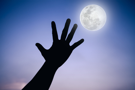 Silhouette of a hand with full moon on fantastic sky background. Symbol is mean to say hi , five , hand up, stop. Outdoors. Outdoor. Cool colors tone photo effect.の写真素材