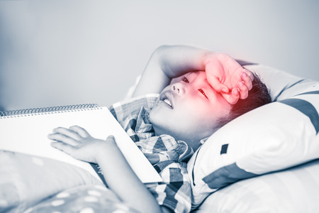 Tired and bored kid unhappy when he read book. Children read and study hard, tired student, education concept. Asian boy have a headache. Red spot indicating location of pain.の写真素材