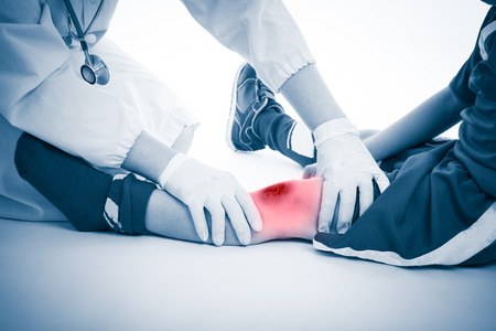 Youth soccer player knee pain, on white background. Doctor checking and give first aid at knee patient. Photo with color increase blue skin and red spot indicating location of pain.の写真素材
