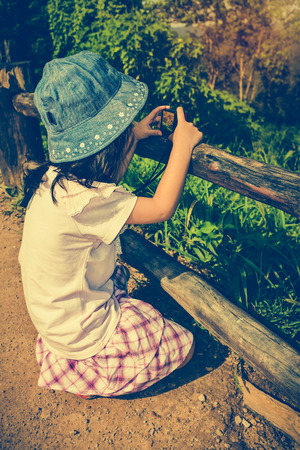 Side view of asian girl with camera at park. Child photographing views nature background. Child relaxing outdoors with bright sunlight at the daytime, travel on vacation. Vintage tone effect.の写真素材