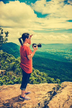 Asian woman photographed the beautiful view by digital camera at view point on mountain. Pretty sky with cloudy, outdoor  on summer day, tropical evergreen forest. Cross process and vintage tone effect.の写真素材