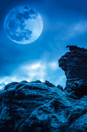 Boulder with blue sky background and beautiful full moon behind cloud at night. Outdoor at nighttime. Beauty of nature use as background.の写真素材
