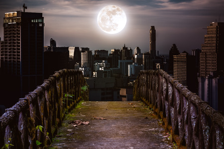 Old concrete bridge with wooden across to skyscrapers with super moon background at night. Dark tone and high contrast style. Vintage tone. The moon were NOT furnished by NASA.の写真素材