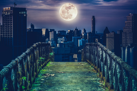 Old concrete bridge with wooden across to skyscrapers with super moon background at night. Dark tone and high contrast style. Cross process style. The moon were NOT furnished by NASA.の写真素材