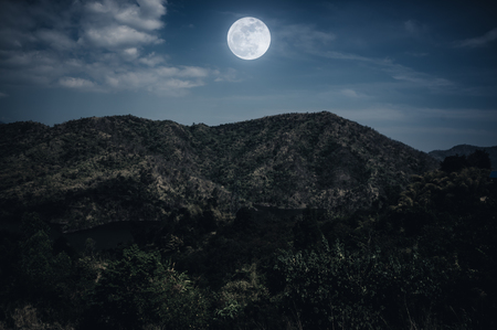 Landscape of night sky and cloudy above mountain peak. Beautiful bright full moon over tranquil nature on dark tone. The moon were NOT furnished by NASA.の写真素材