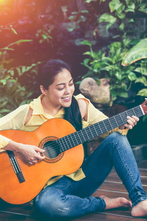 Pretty songwriter smiling and having fun enjoy hobby concept. Asian woman playing acoustic guitar, outdoor at daytime with bright sunlight on summer day.の写真素材