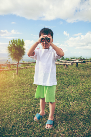 Asian boy looking through a telescope, among of nature and blue sky. Child relaxing holiday. Concept about outdoors for children on summer day with bright sunlight. Travel on vacation. Vintage tone.の写真素材