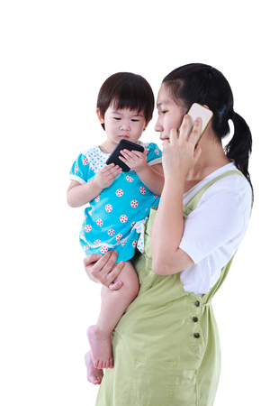 Busy asian mother using smartphone and carrying her daughter. Lovely girl using electronic gadget.の写真素材