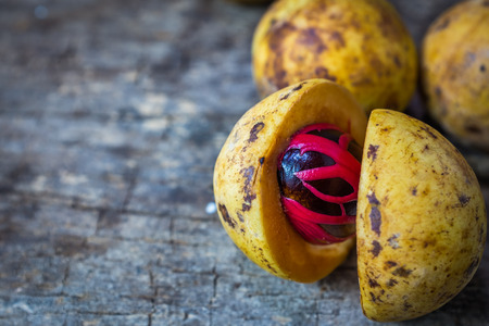 Pile of fresh nutmeg fruit with red placenta-like cover of seed of myristica fragrant, medicinal properties. Tropical colorful plant on wooden background with copy space.の写真素材