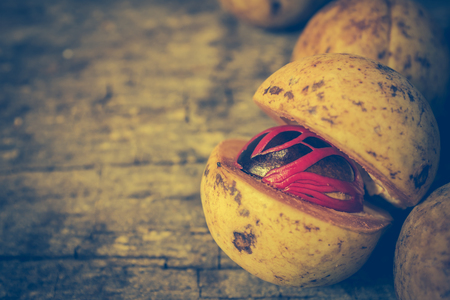 Closeup fresh nutmeg fruit with red placenta-like cover of seed of myristica fragrant, medicinal properties. Tropical colorful plant on wooden background. Vintage effect tone.の写真素材