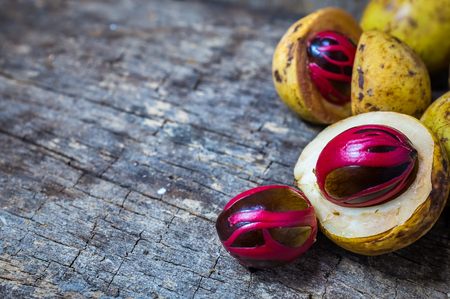 Pile of fresh nutmeg fruit with red placenta-like cover of seed of myristica fragrant, medicinal properties. Tropical colorful plant on wooden background with copy space.の写真素材